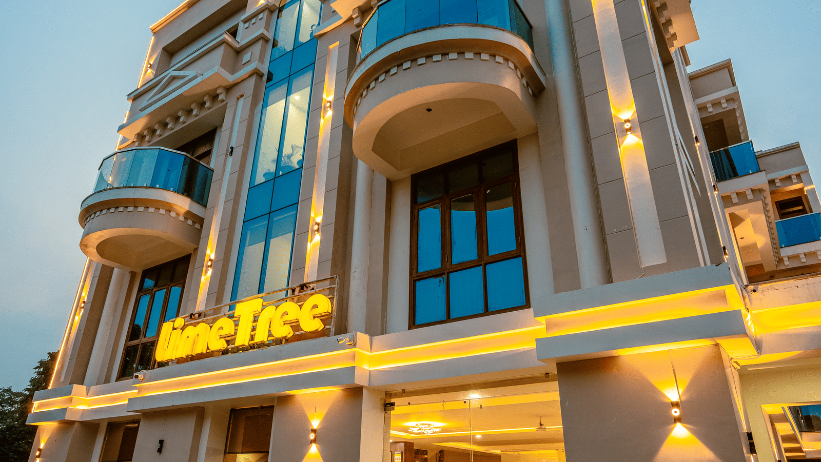 Vertical view of an ornate multiple storey building exterior of Lime Tree Hotels & Service Apartment Private Limited featuring illuminated columns.