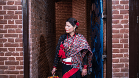 A woman in elegant attire walking through a traditional wooden doorway of a red brick heritage building in Bhaktapur, Nepal.