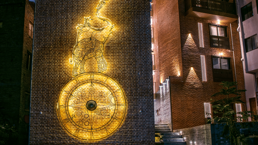 Evening view of a historic brick tower wall featuring an illuminated golden relief map sculpture at a luxury hotel in Bhaktapur, Nepal.