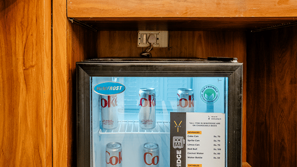 Compact black mini fridge stocked with beverages, built into a wooden hotel cabinet.