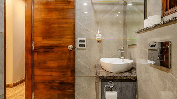 Compact ensuite bathroom showing a white ceramic toilet, a modern vanity sink unit, and a rich wood-panelled door.