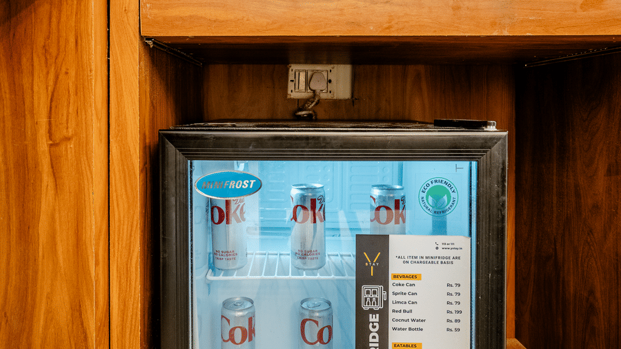 Compact black mini fridge stocked with beverages, built into a wooden hotel cabinet.