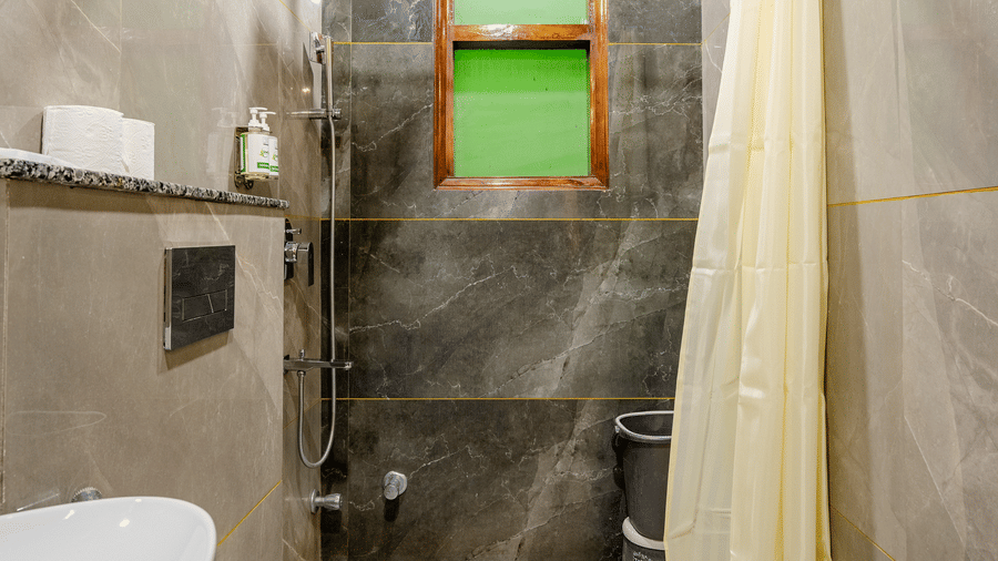Long, compact hotel bathroom featuring a white sink, modern toilet, and grey wall tiles with a shower curtain.