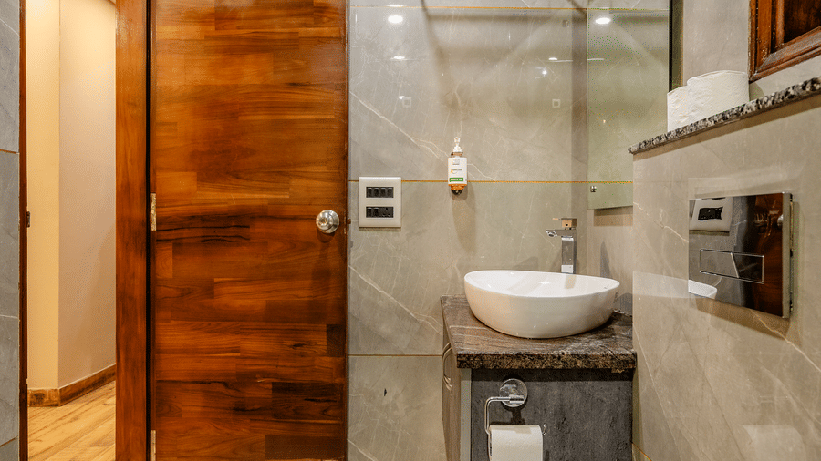Compact ensuite bathroom showing a white ceramic toilet, a modern vanity sink unit, and a rich wood-panelled door.