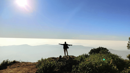 Trekker standing with outstretched arms at the Baba Budangiri viewpoint overlooking the Western Ghats.