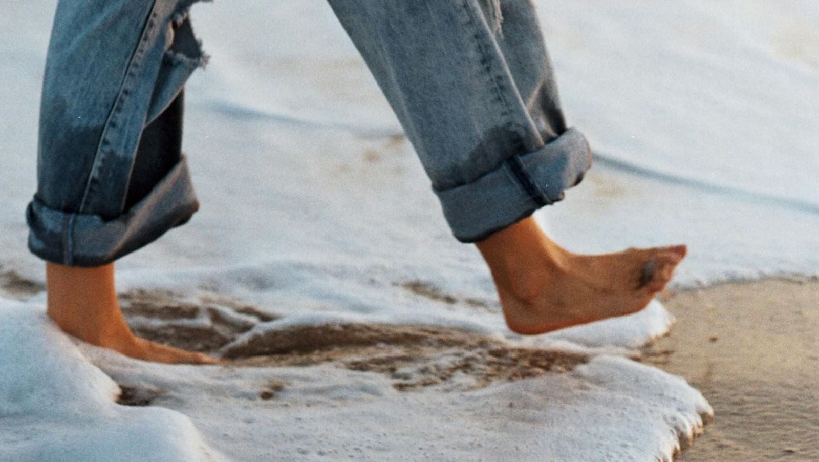 A person walking on a beach barefoot while pulling her pants up.