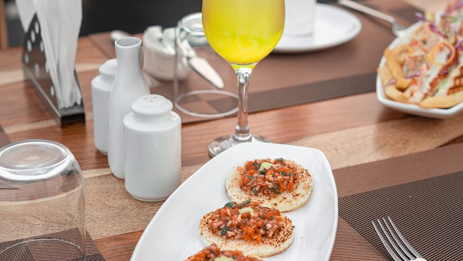 A pineapple mocktail with bruschetta on a wooden table by the poolside at The Bridge, Clarks Inn Suites Jaipur