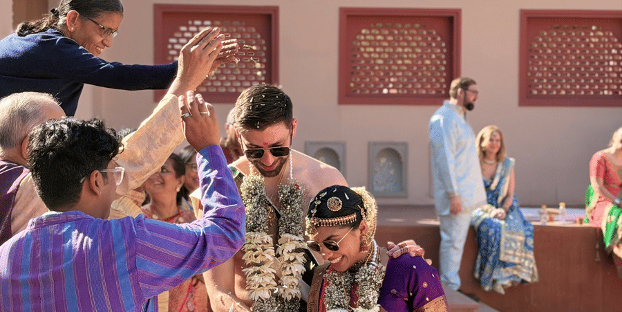 Wedding guests joyfully tossing flower petals over a couple during a daytime celebration at Umaid Palace.