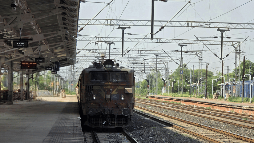 An electric train arrives at a nearly empty railway station under a clear sky, with overhead electric lines visible | Chennai to Pudukkottai train