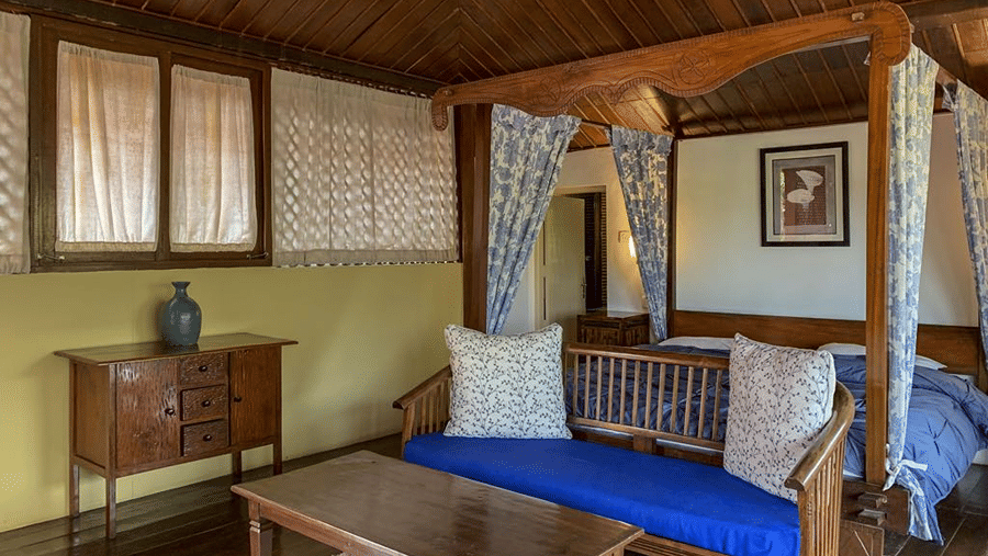 Cosy room with a blue-cushioned sofa, wooden furnishings, framed artwork and a view through the windows.