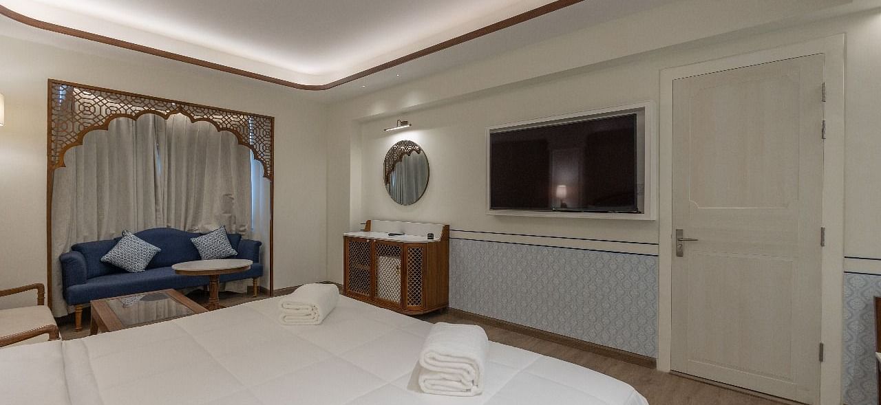 A wide angle shot of the Triveni Room with a luxurious double bed facing a wall mounted television at Bhagirathi by RDB Atishay.
