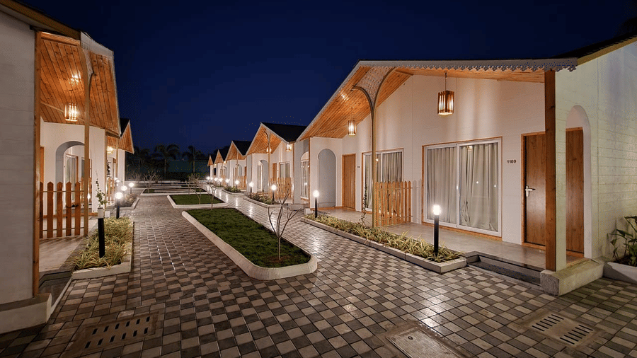 A view of the cobbled walkway with manicured lawn in the centre and Cottages on either side, as seen during the night at VITS Daman Devka Beach, the hotel provides the best accommodation in Daman.