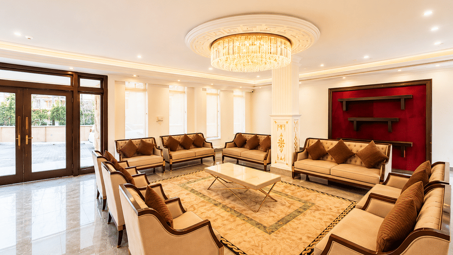 Hotel lobby lounge with beige sofas set around a patterned rug, a glass chandelier overhead, red accent walls and polished marble flooring below.