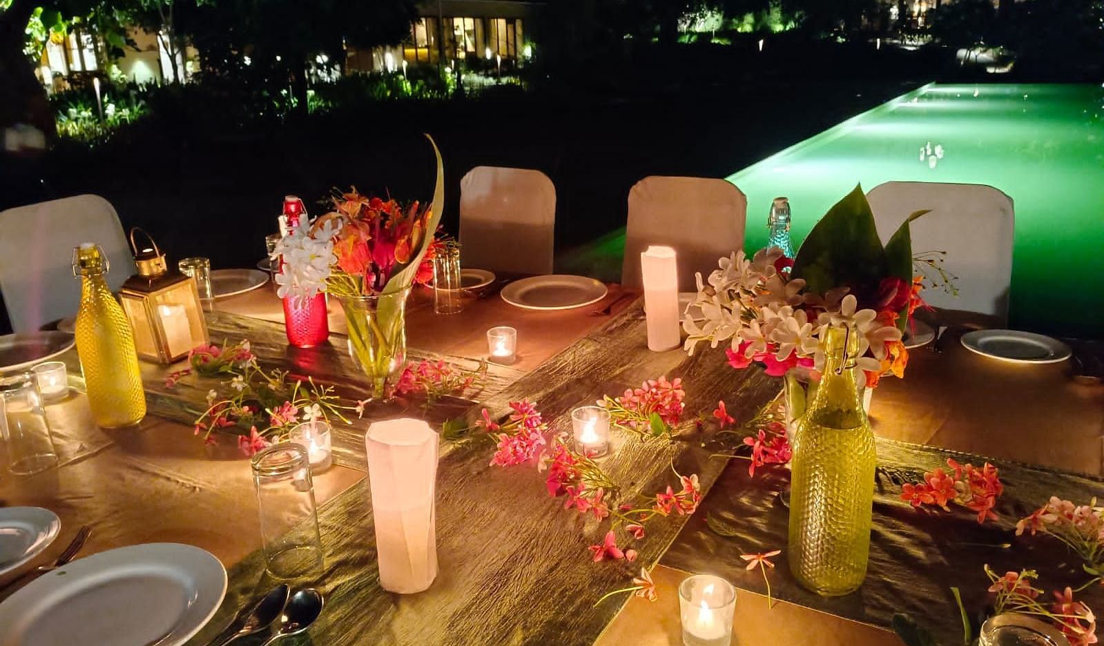 A romantic candlelit dining arrangement besides the outdoor swimming pool at Saraca Resort & Spa Corbett at night