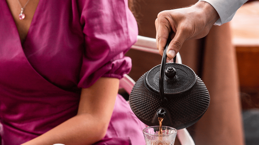 Waiter pouring black tea into a traditional pear-shaped glass in front of a woman seated at the table.