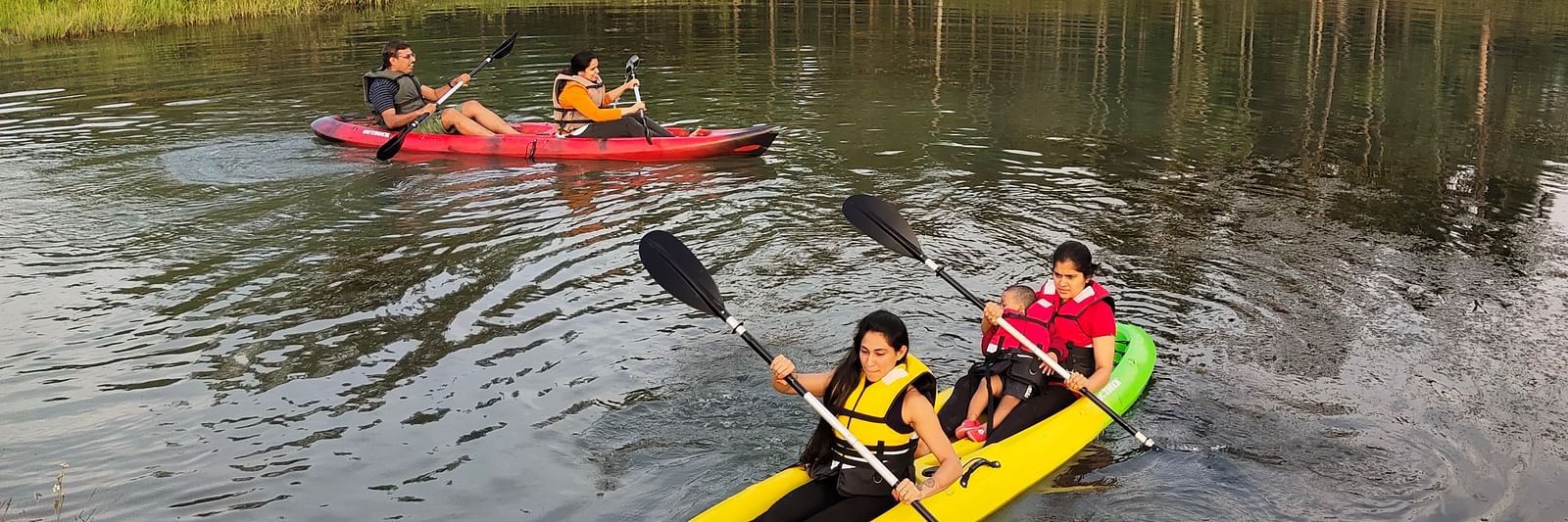 People in life jackets paddling kayaks on a serene river with dense forest in the background - Evergreen County
