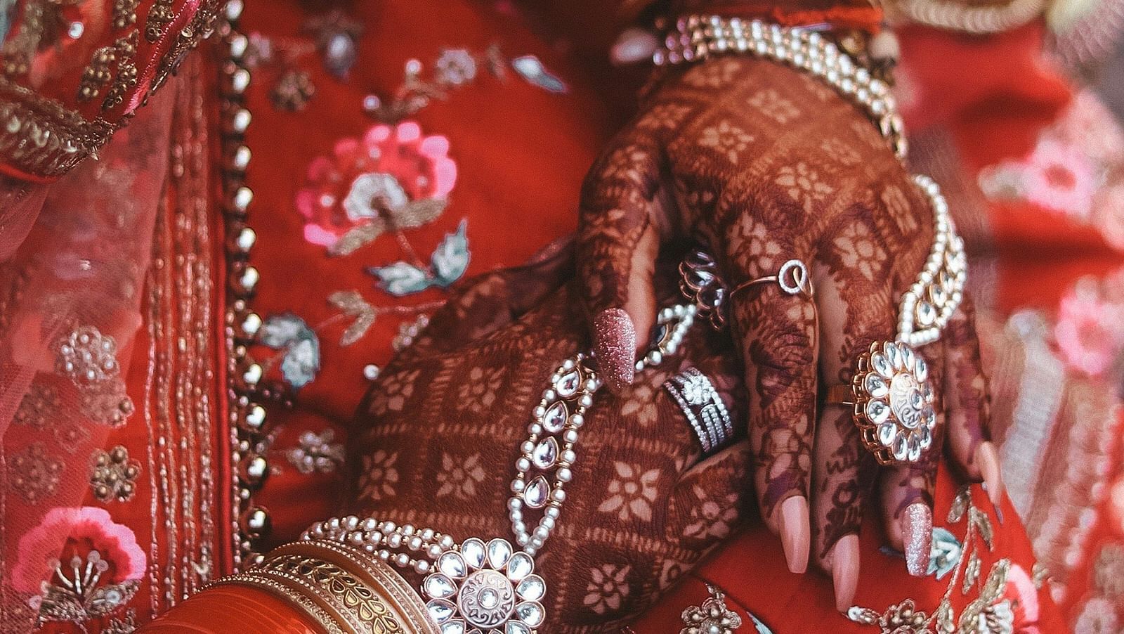 A top-down view of a woman in traditional attire, with her hands adorned with mehendi art resting on her lap.