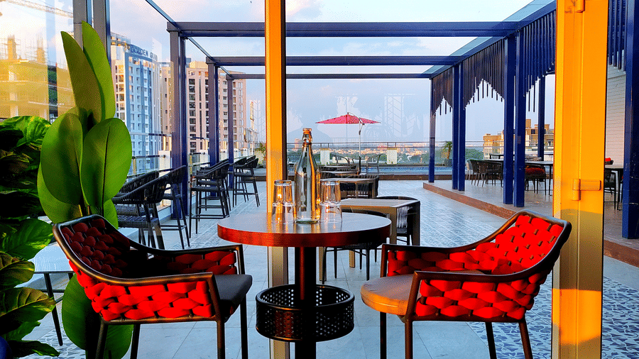 Close up of 2 elevated chairs facing each other with a glass partition beside it overlooking the rooftop from Kensho at Leroy Grand, Yeshwanthpur.