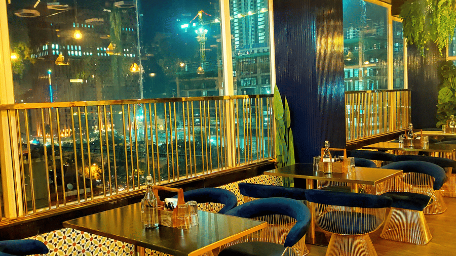 Side view of the well-arranged dining tables besides the window at Kensho rooftop pub with warm lighting at Leroy Grand, Yeshawanthpur.