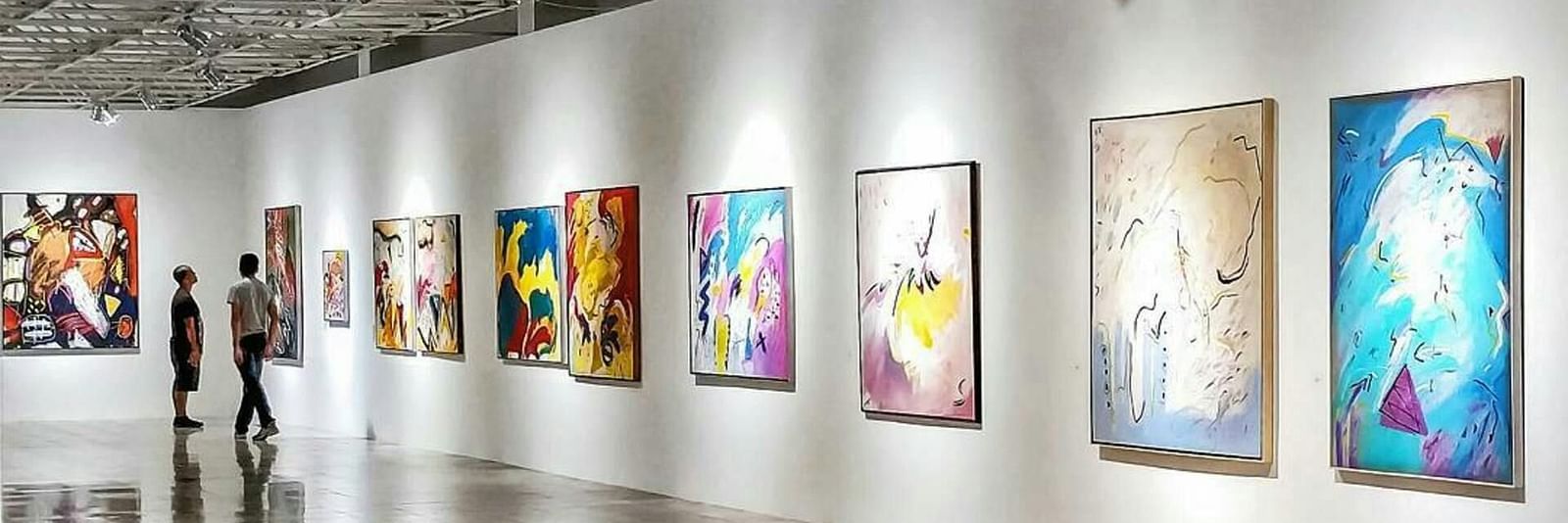 A brightly lit art gallery with white walls and several framed pieces displayed along the length of the room.