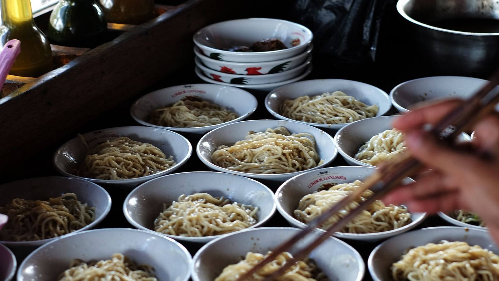A close up of many bowls of noodles kept next to each other with a person standing next to it.
