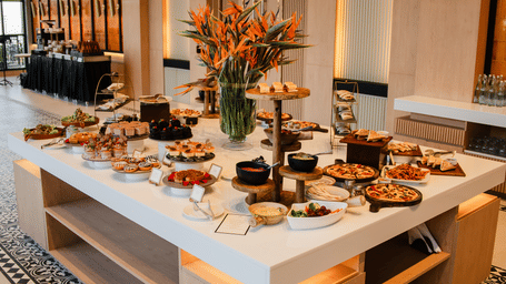 Buffet island at Polo Resort Cherrapunji with assorted dishes, pastries, bird-of-paradise centerpiece and patterned tile floor border.