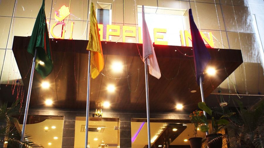 A view of the hotel from the front illuminated by warm yellow lighting and with flags placed in the front - TGI Apple Inn, Jaipur 