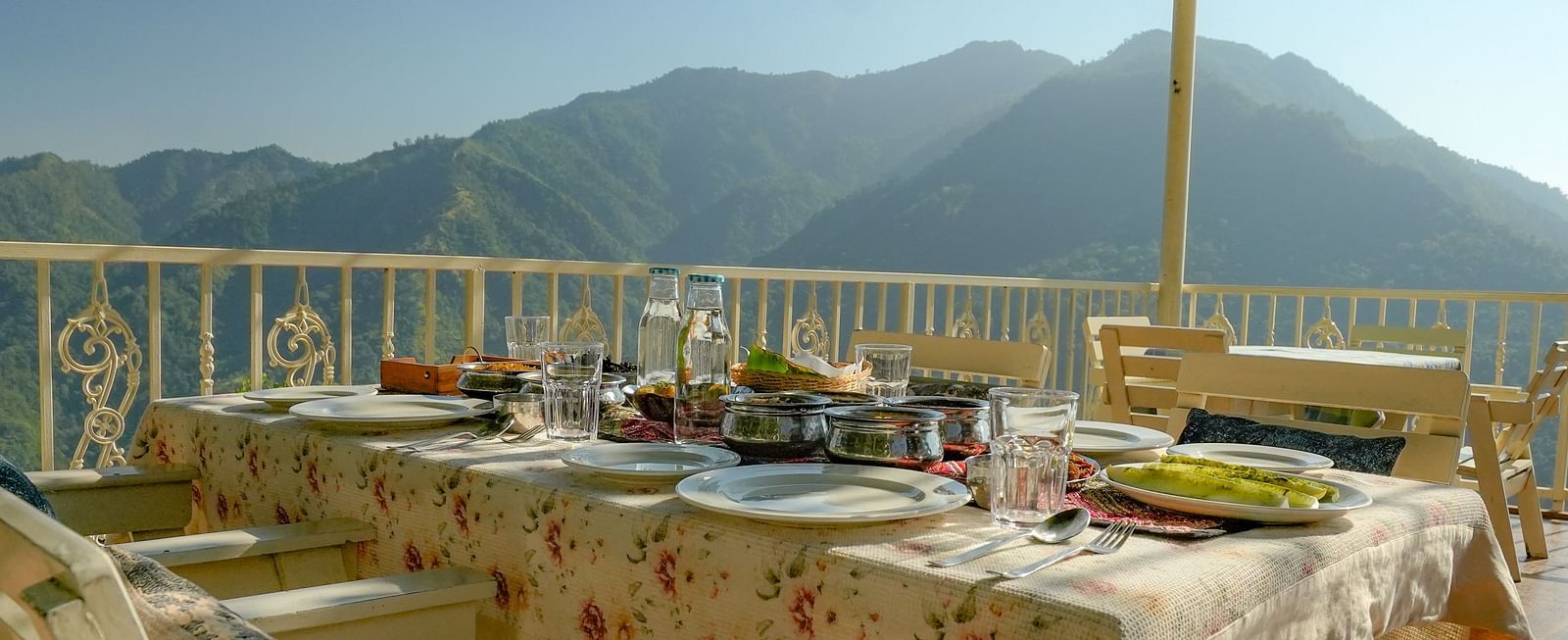 A corner view of the rooftop restaurant at Neer Ganga, featuring a dining area with a roof covered in creeping plants, offering a scenic mountain view.