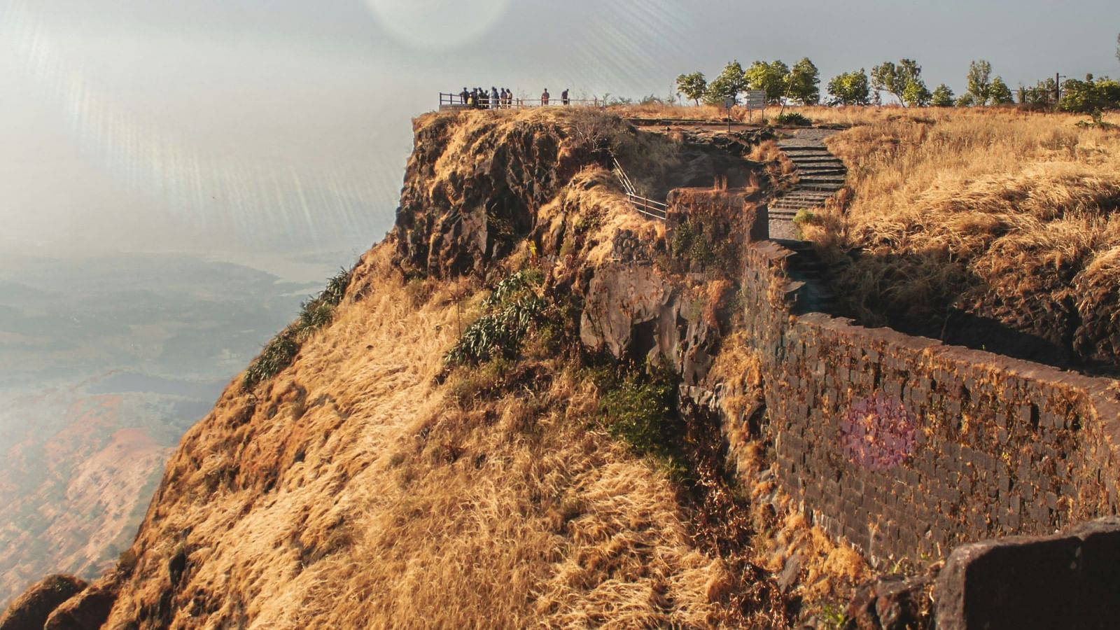 An aerial view of a historic fort wall on a hill, with a clear sky and sun lens flare.