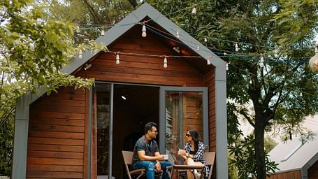 A couple sits outside the cottage room, chatting and enjoying the surrounding natural view at Crescent Spa & Resort, Indore