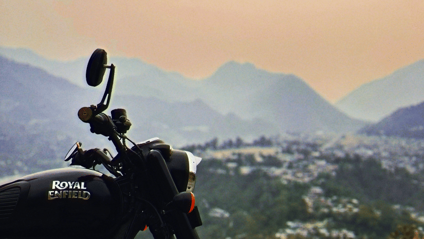 A motorbike with the label Royal Enfield halted outdoor with silhouette of mountains in the background