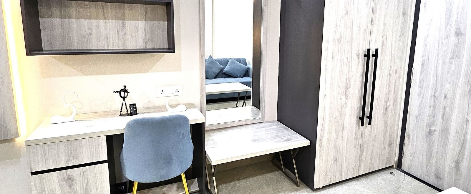 Modern workspace in a studio room featuring a sleek desk with storage, a comfortable upholstered chair, open shelves, a full-length mirror with a bench, and a spacious wardrobe for added convenience - Urban Suites by BluSalzz, Jaipur