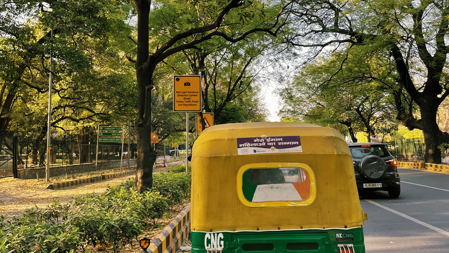 An auto-rickshaw near a tree-lined road with a pedestrian sign on the side