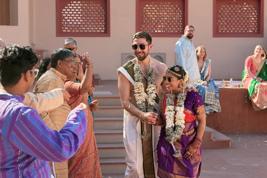 A bride and groom dressed in traditional attire walk past wedding guests during a daytime courtyard ceremony at Umaid Palace.