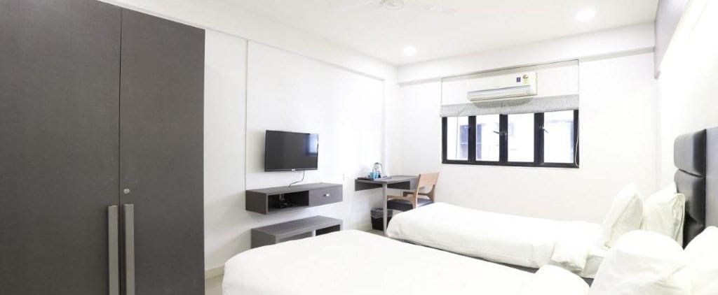 Corner view shot of the Premium Twin Room at Pravasa Ahmedabad featuring bright and minimalist interiors along with a wardrobe in the corner.