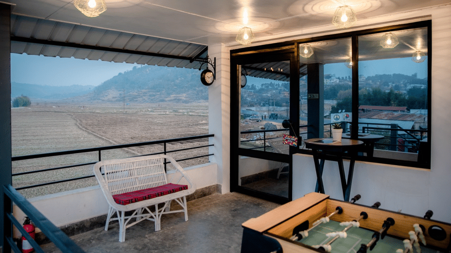 Covered balcony lounge at Woodstock Resort with seating, a foosball table, hanging lights, and large windows overlooking hills and an open landscape.