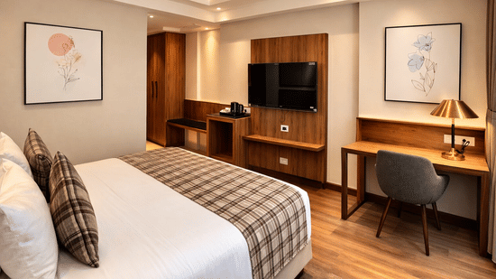 Bedroom at Pride Premier Darjeeling featuring a bed, a flat TV screen mounted on the wall, work desk and chair, and tea and coffee maker.