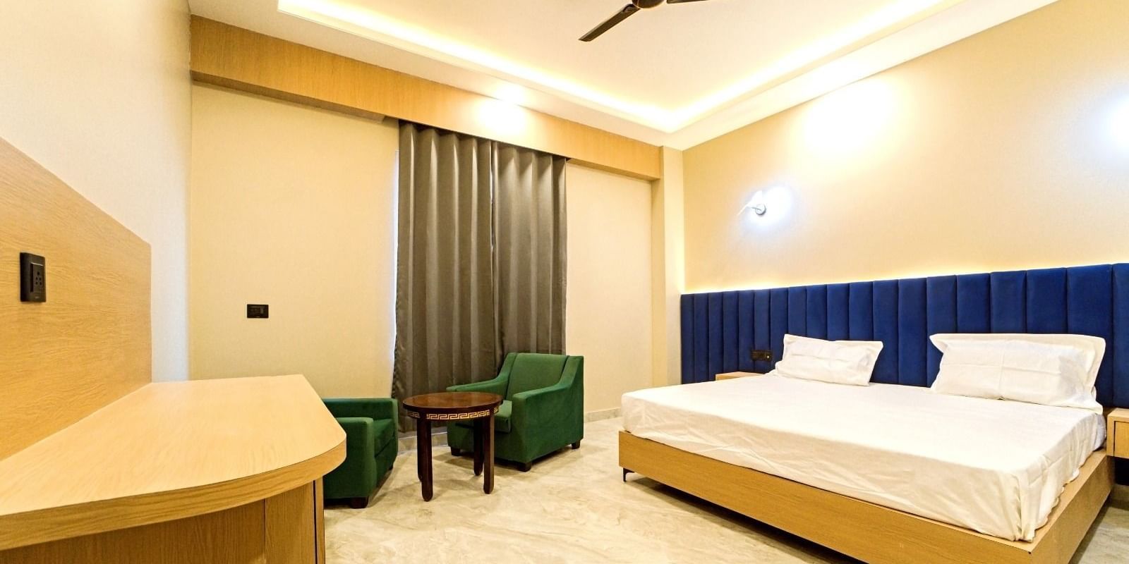 Modern guest room at Grassfield Riveria Resort, Jaipur, featuring a large bed, seating area, ceiling fan, and warm lighting.