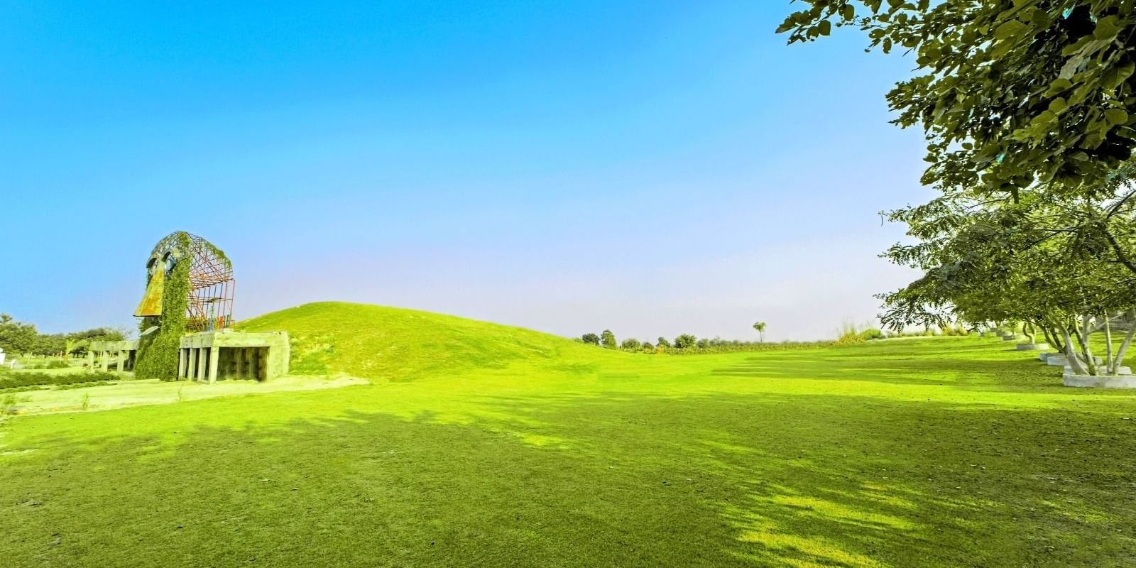 Vast lawn with the artistic mask sculpture of Grassfield Riveria Resort, Jaipur, set against a clear sky.