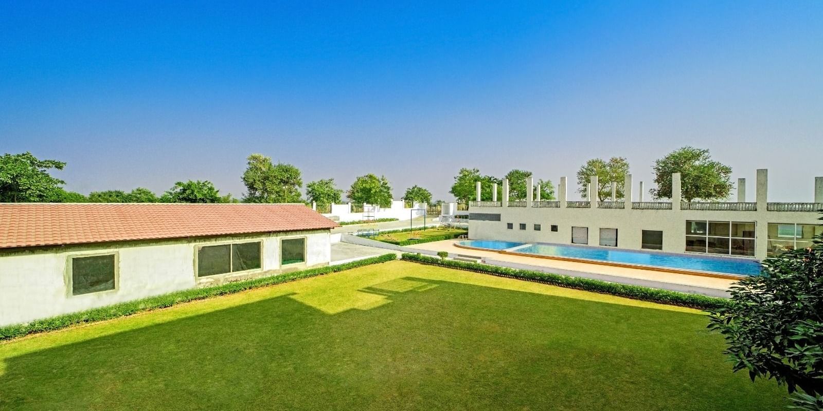 Expansive lawn with a swimming pool and buildings in the background at Grassfield Riveria Resort, Jaipur.