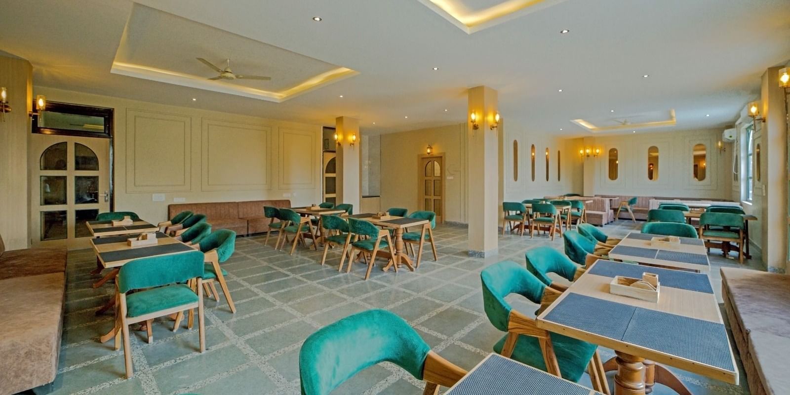 Elegant dining area at Grassfield Riveria Resort, Jaipur, with teal upholstered chairs, wooden tables, and warm lighting.