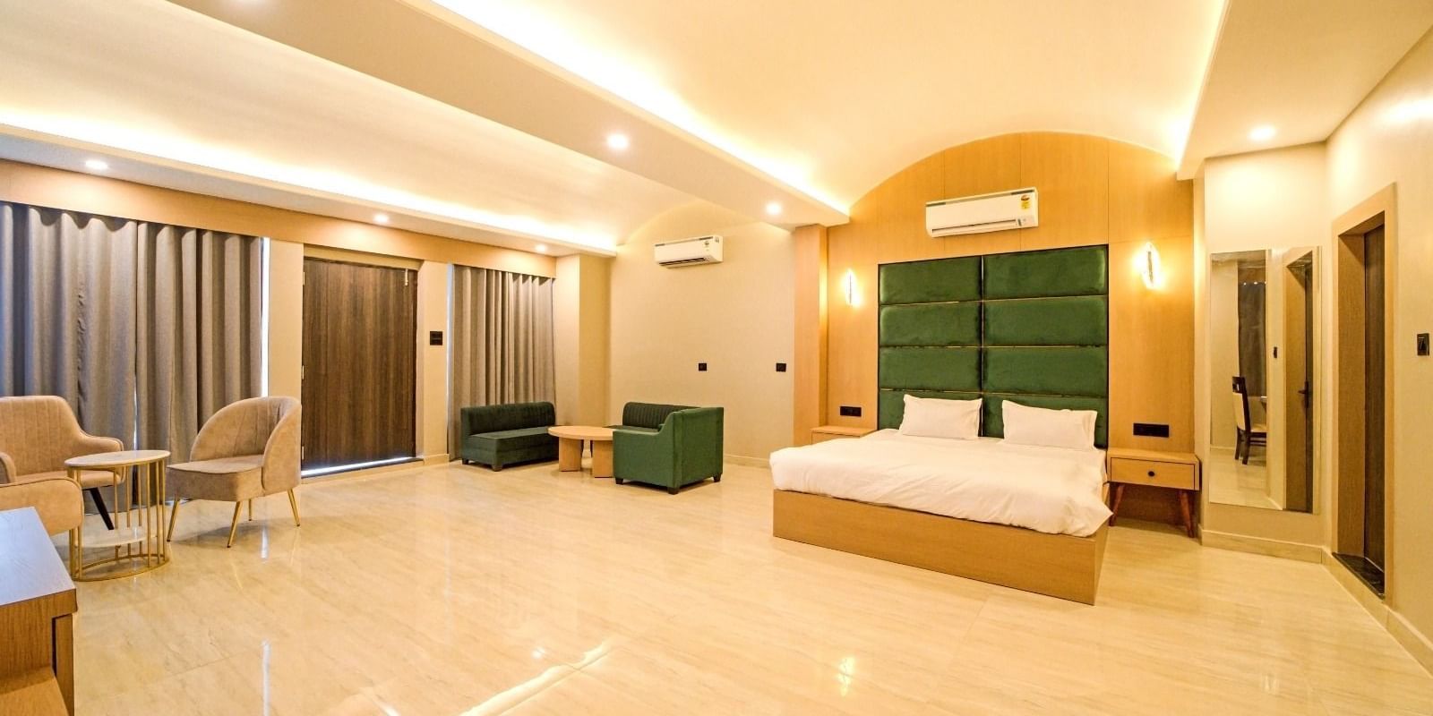 Spacious bedroom at Grassfield Riveria Resort, Jaipur, featuring a large bed, seating area, modern lighting, and floor-to-ceiling curtains.