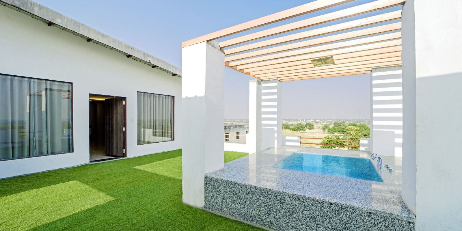 Poolside lounge area at Grassfield Riveria Resort, Jaipur, featuring a shaded seating space and views of the swimming pool.
