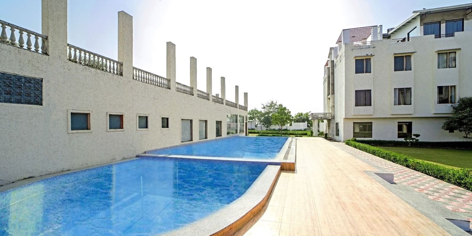 Outdoor swimming pool at Grassfield Riveria Resort, Jaipur, featuring clear water and a wooden deck under bright sunlight.