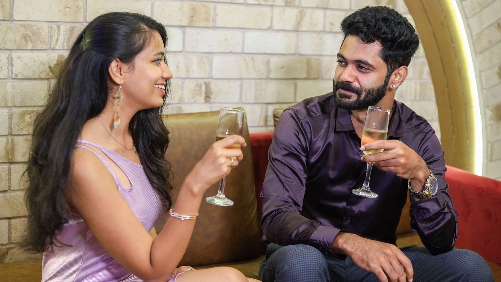 A man and woman sit on a couch in a modern lounge, smiling at each other while holding wine glasses and toasting at Jenneys Residency
