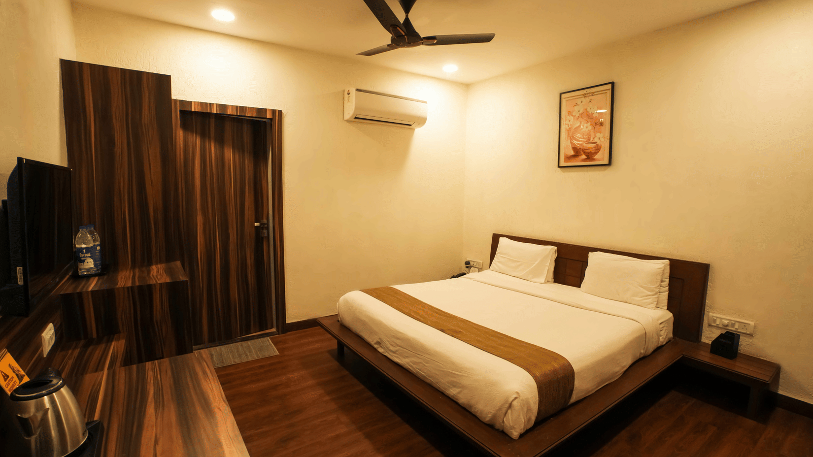 Interior view of a bedroom at Adamo The Village featuring a  double bed, dark wooden flooring, and a ceiling fan.