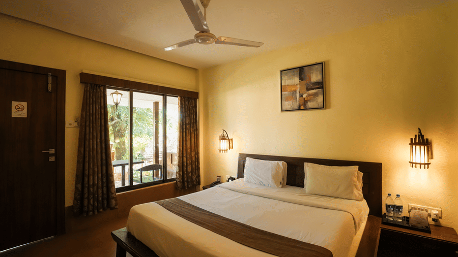 A resort bedroom featuring a double bed, large window with drapes, and ambient hanging wall lanterns.