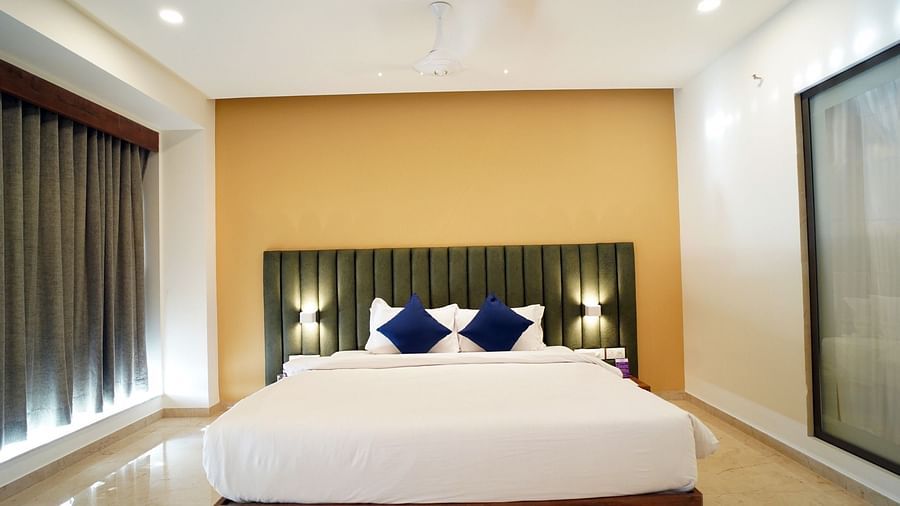 A queen-size bed in well-lit Queen Suite Room with navy blue cushions and blinds