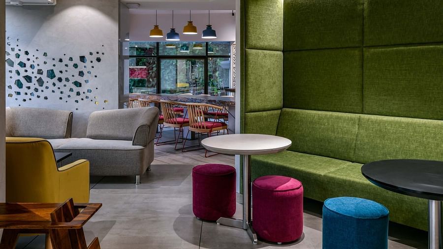 Large cushioned booth seating with a round table, alongside cylindrical cushion seating and additional sofas placed towards the side, at Indie Stays, BKC Kalina.