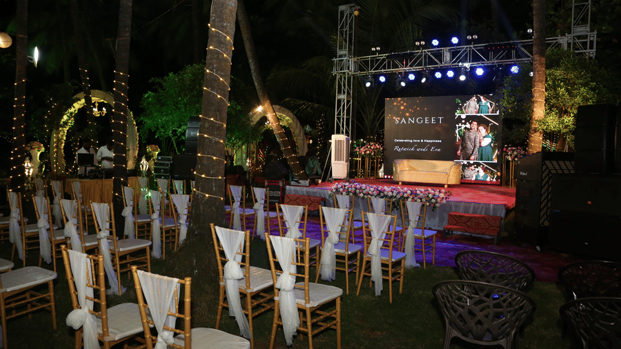 Outdoor seating with white chairs arranged before decorated stage at Paradise Lagoon Resort, Udupi.